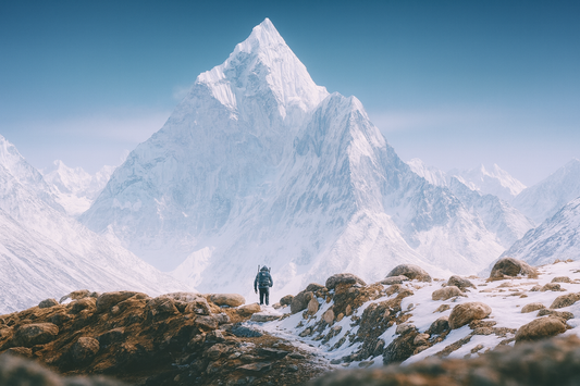 Une personne en tenue de randonnée avance vers une immense montagne enneigée dans un paysage glacial