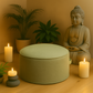 Coussin de méditation vert doux entouré de bougies et de plantes, ambiance relaxante avec statue de Bouddha