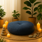 Coussin de méditation bleu ardoise dans un décor apaisant avec bougies, galets et plantes vertes, atmosphère zen