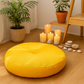 Coussin de méditation jaune entouré de bougies allumées, galets et plantes dans un coin zen et chaleureux