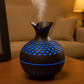 Diffuseur d’huiles essentielles en bois foncé avec éclairage LED bleu, diffusant une brume fine dans un salon tamisé en soirée.