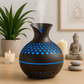 Diffuseur d’huiles essentielles en bois foncé avec éclairage bleu, posé sur une table près de bougies et d'une statue de méditation.